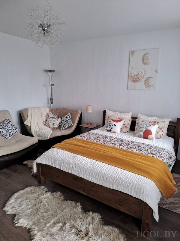 Уютная спальня с деревянной кроватью, цветочным покрывалом, креслами с пледами и абстрактной люстрой.