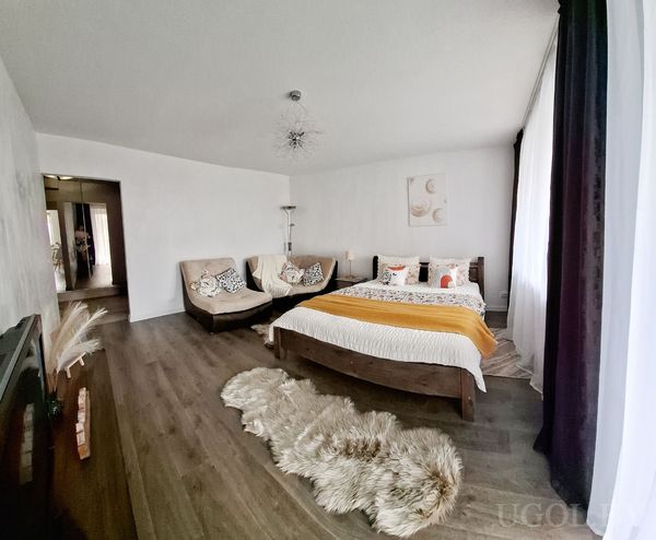 Современная спальня с бело-оранжевым текстилем, диваном с подушками, пушистым ковром и настенным декором с кругами.