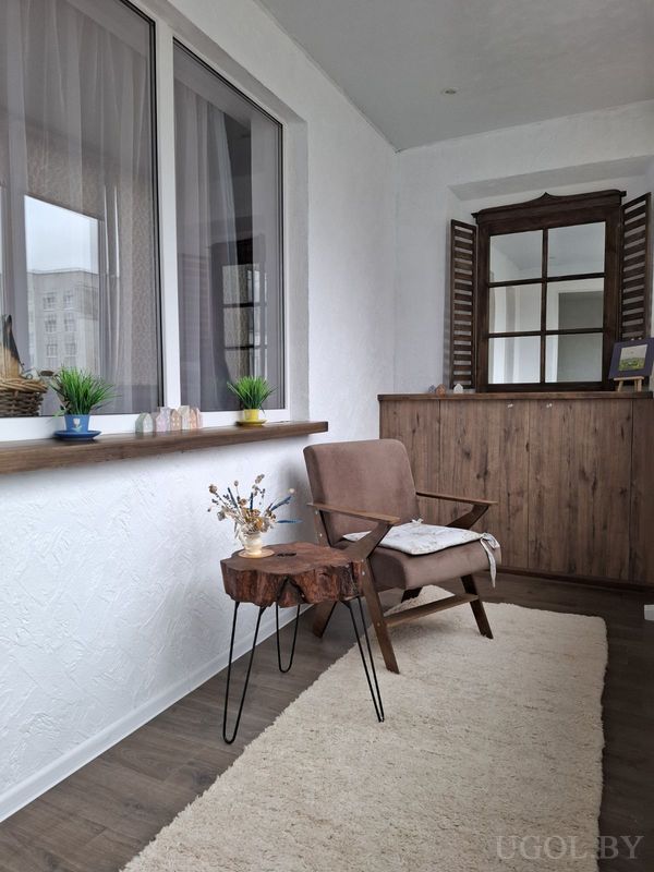 Уютный уголок с креслом, столиком из дерева, вазой с сухоцветами и декором на широком подоконнике.