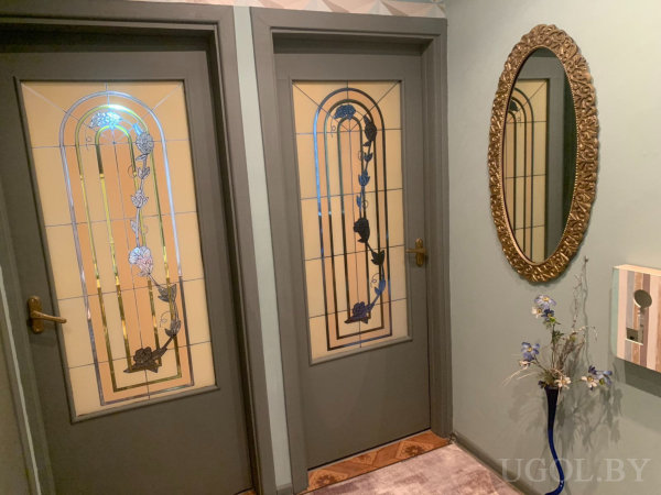 Интерьер с двумя дверями, витражами, зеркалом, вазой с цветами и декоративным ящиком.