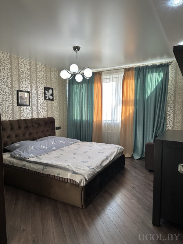 Светлая комната с большой кроватью, коричневым изголовьем, акцентными шторами и стильной люстрой.