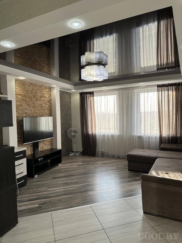 Секционный диван, телевизор на фоне декоративного камня, светлая плитка и тёмный ламинат.