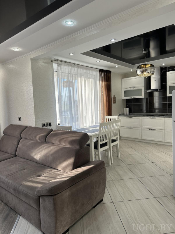 Серая мягкая мебель, белая столовая группа, кухня с чёрным фартуком и глянцевым чёрным потолком.