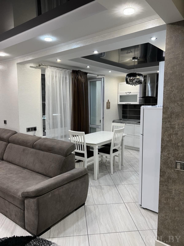 Белая мебель, серый диван, плитка с узором, акцентный потолок и тёмные шторы у окна.