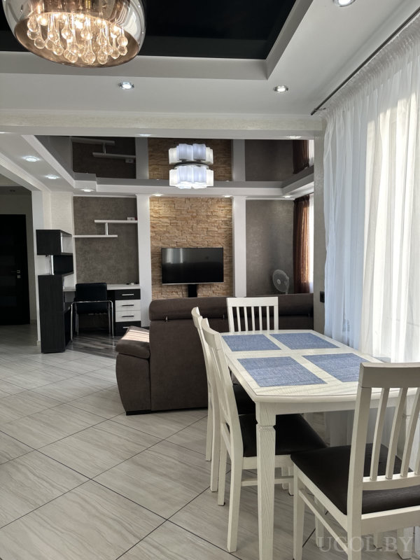 Белый стол с синим декором, коричневый диван, ТВ-зона с камнем и встроенная рабочая зона.