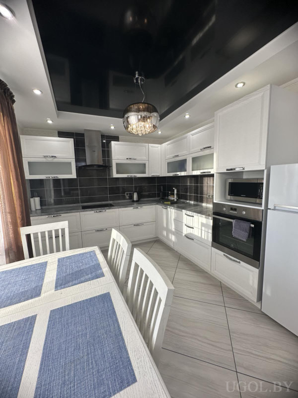 Белые шкафы, чёрный фартук, встроенная техника, стол с синими подставками и диагональная плитка.