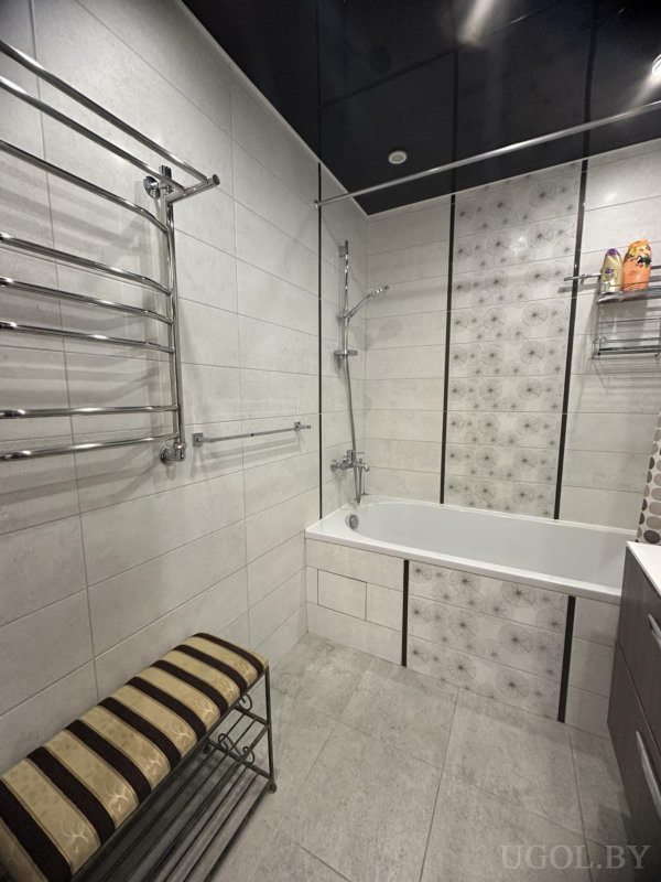 Белая ванна, душ, цветочные вставки на стене, металлические держатели и мягкая скамья.