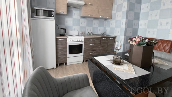 Белый холодильник с микроволновкой, плита, раковина и глянцевый чёрный стол с сервировкой и цветочной композицией.