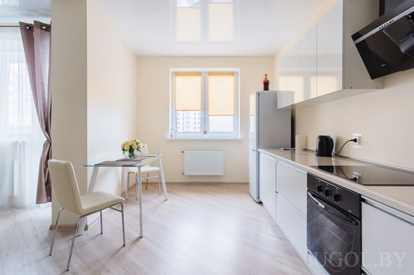 Современная кухня с белыми шкафами, плитой, холодильником, телевизором и стеклянным столом с цветами.