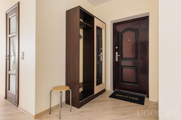 Аккуратная прихожая с зеркальным шкафом, входной дверью с номером 8, круглым табуретом и ковриком Welcome.