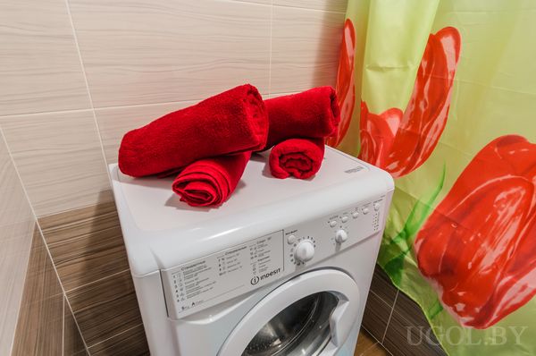 Белая стиральная машина Indesit с аккуратно сложенными красными полотенцами и занавеской с красными тюльпанами.