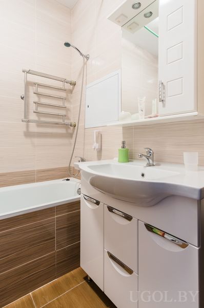 Современная ванная с белой ванной, умывальником с тумбой, зеркальным шкафчиком и полотенцесушителем.