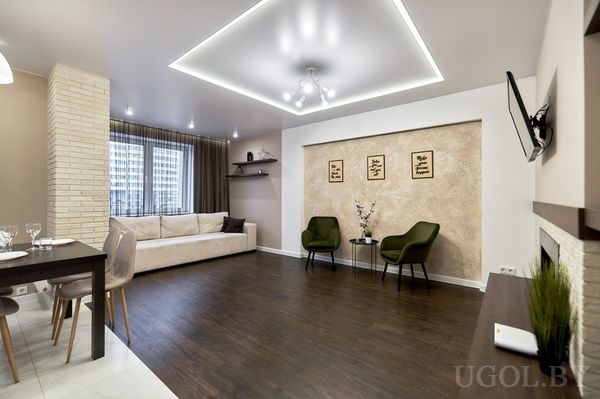 Современная гостиная с диваном, зелёными креслами, камином с белой отделкой, телевизором и тёмным деревянным полом.