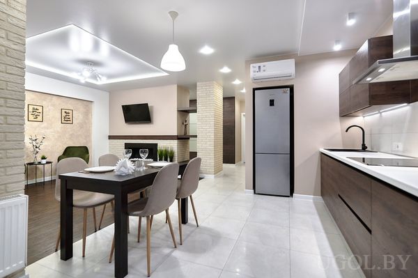 Кухня с тёмными фасадами, белой столешницей, столом на четверых и видом на гостиную с зелёным креслом.