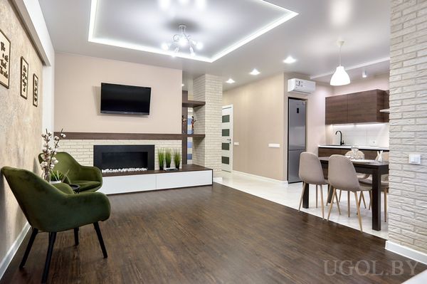 Открытая зона с камином, телевизором, кухней с техникой и столом с четырьмя стульями под подвесным светильником.