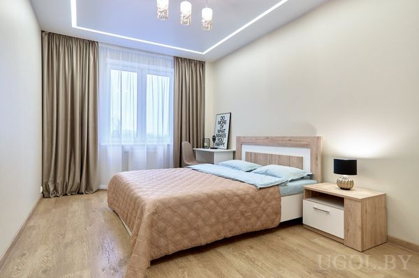 Минималистичная спальня с бежевым покрывалом, голубыми подушками, рабочим столом и надписью «DO MORE OF WHAT MAKES YOU HAPPY».