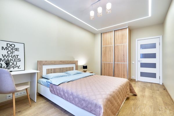 Современная спальня с голубыми подушками, белым столом, встроенным шкафом и белой дверью с матовыми вставками.