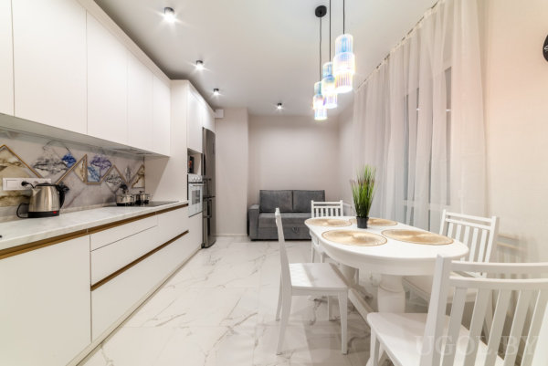 Белые шкафы, геометрический фартук, встроенная техника и обеденная зона с яркими подвесными светильниками.