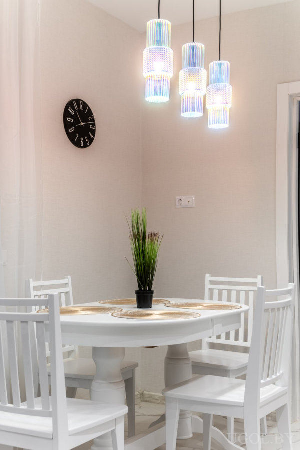 Круглый стол с белыми стульями, подвесные стеклянные светильники и часы с цифрами по спирали на стене.