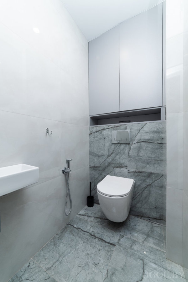 Мраморные стены, встроенный шкаф, маленькая раковина и гигиенический душ в компактном пространстве.