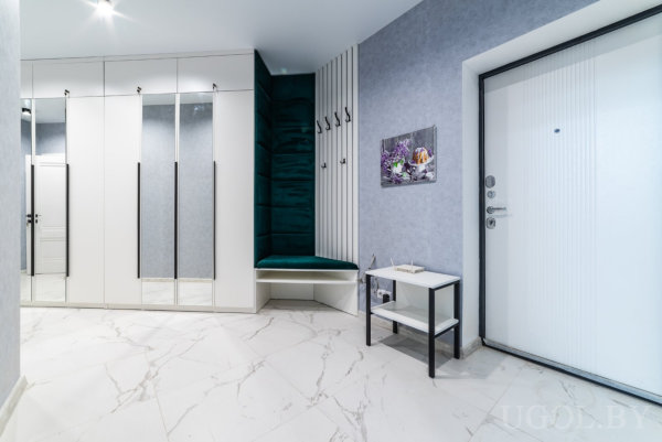 Шкафы с чёрными ручками, зелёная мягкая ниша и белая дверь с декором создают уютный входной ансамбль.