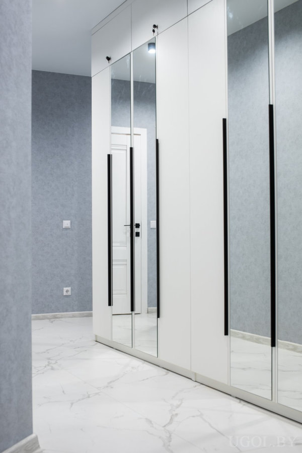 Белые шкафы с чёрными ручками, мраморный пол и мягкий свет в минималистичном оформлении.