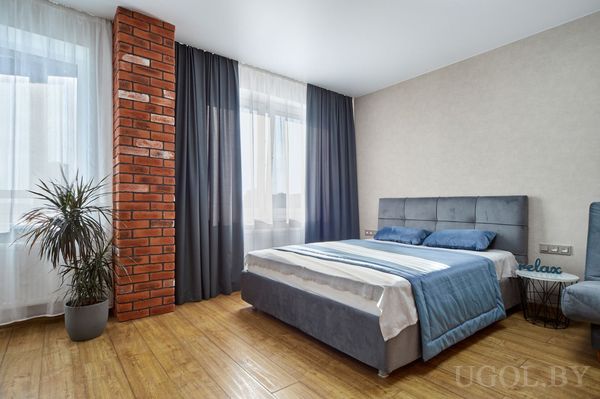 Светлая спальня с серым основанием кровати, голубым текстилем, кирпичной колонной и декором «relax».