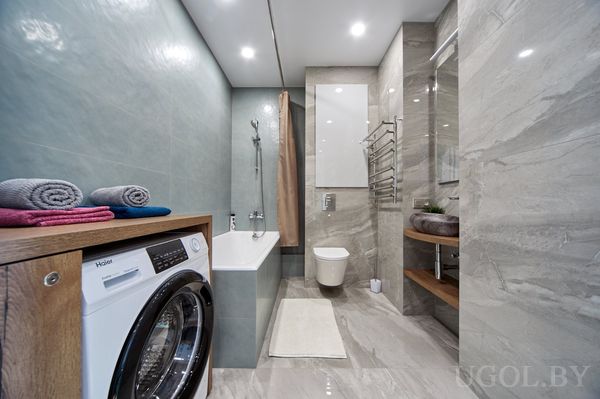 Функциональная ванная с душем, стиральной машиной, комбинированной плиткой и полками с декором.