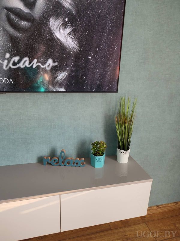 Белый комод с растениями, надписью «relax», постером с женским лицом и бирюзовой стеной.