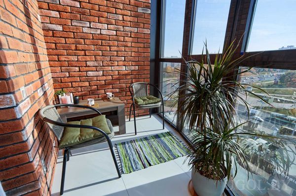 Балкон с креслами, деревянным столом, декором, большим растением и панорамным остеклением.