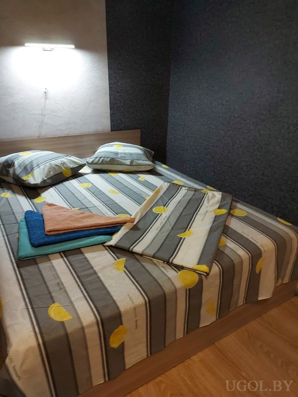 Комната с кроватью, покрывалом с лимонами, тёмными стенами, настенным светильником и стопкой ярких полотенец.