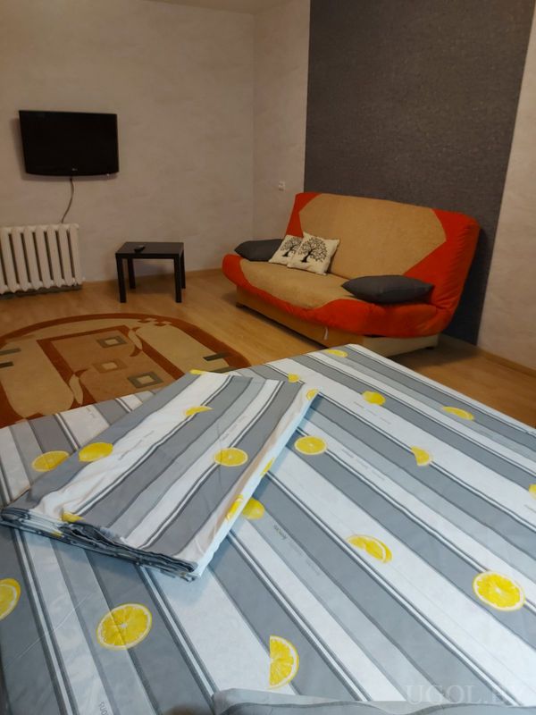 Жилая зона с кроватью, диваном с подушками, журнальным столиком, телевизором и ковром с геометричным узором.