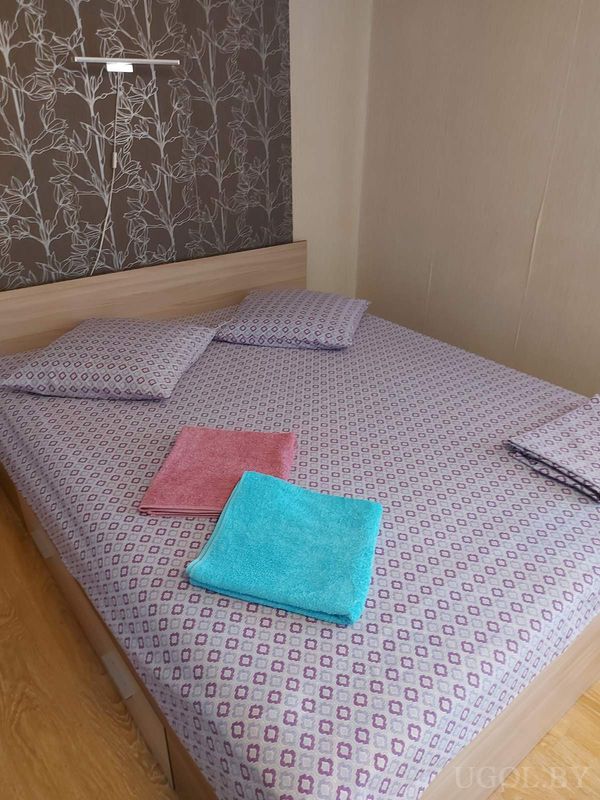 Комната с деревянной кроватью, настенным светильником, обоями с цветами и аккуратно сложенными полотенцами.