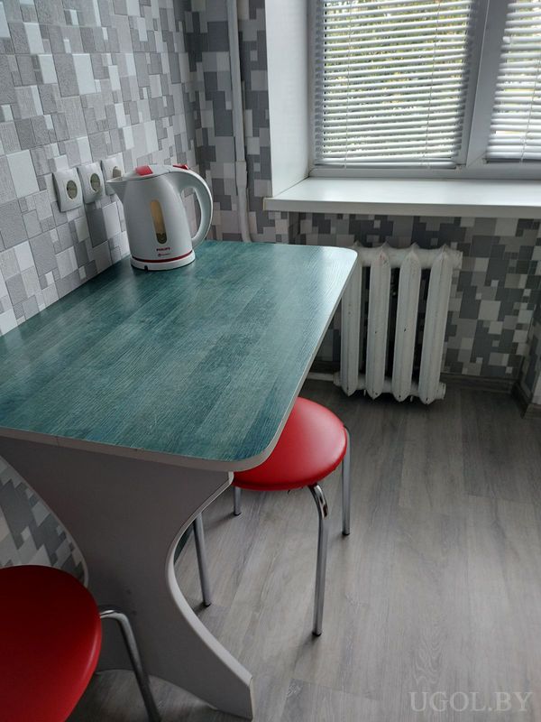 Уголок с столом, чайником, геометричной плиткой на стене и окнами с горизонтальными жалюзи.