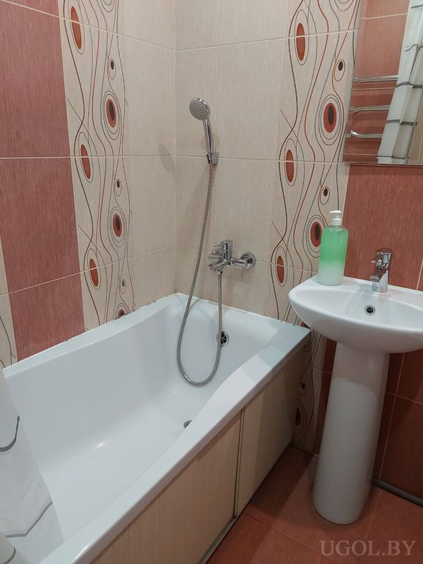 Интерьер с ванной, раковиной, зеркалом, плиткой с волнистыми узорами и дозатором на умывальнике.