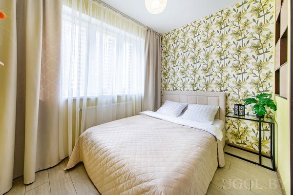 Уютная спальня с бело-оранжевым текстилем, диваном с подушками, пушистым ковром и настенным декором с кругами.