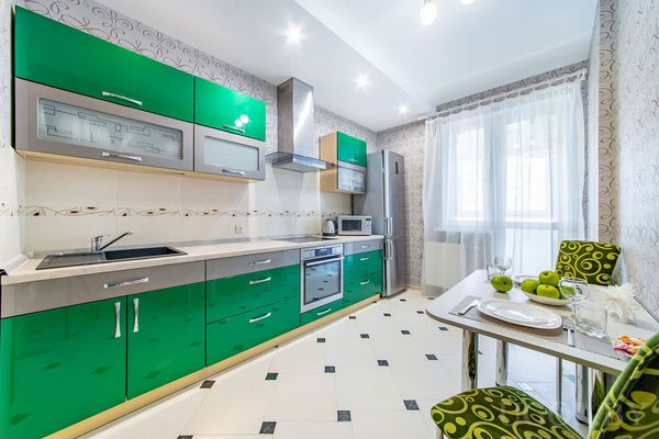 Яркая кухня с зелёными фасадами, техникой, столом на двоих и зелёными акцентами в текстиле и декоре.