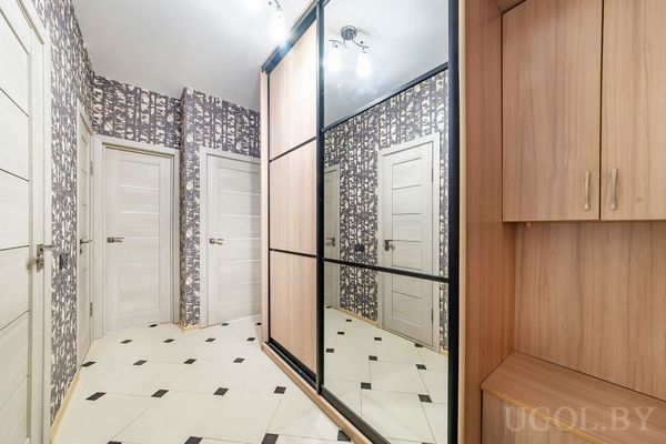 Современный коридор с белыми дверями, зеркальным шкафом, тёмными обоями с ветками и светлой плиткой.