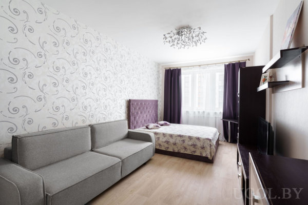 Интерьер с кроватью, диваном, телевизором, люстрой, тюлем и обоями с завитками.