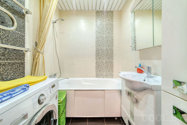 Комната с ванной, умывальником, зеркалом, машиной, корзиной и плиткой с вертикальным узором.