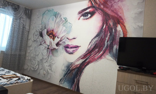 Комната с кроватью, телевизором на тумбе, панно с женским лицом, тюлем и светлым покрытием пола.