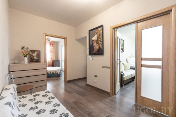 Проход с тёмным полом, скамьей, вазой, картинами и видом на две спальни с разными шторами и текстилем.