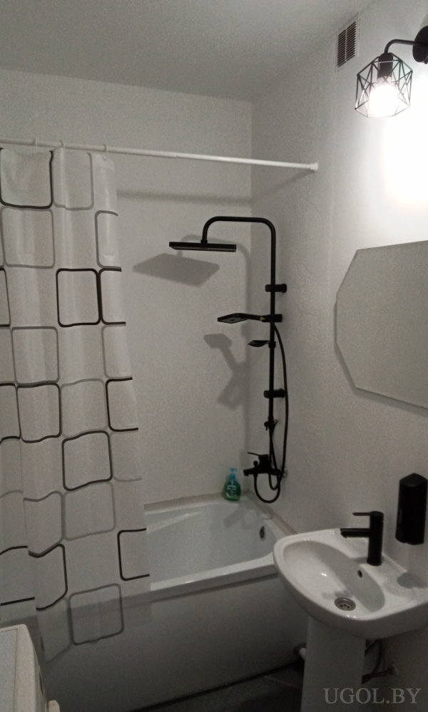 Комната с ванной, умывальником, чёрным смесителем, зеркалом и шторкой с квадратным узором.