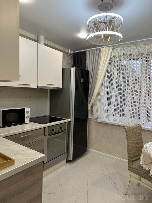 Современная кухня с белыми и деревянными фасадами, плитой, микроволновкой, круглым столом с кружевной скатертью и многослойными шторами.