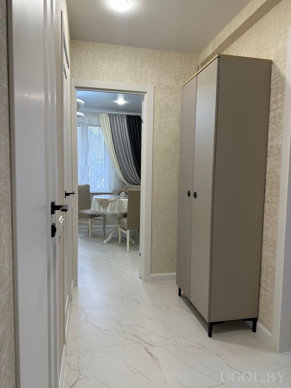 Светлый коридор с белыми дверями, мраморным полом, высоким шкафом и выходом в столовую с круглым столом и шторами.
