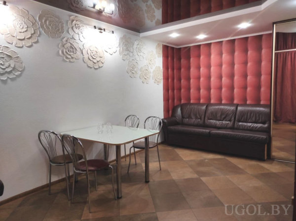 Белый стол с металлическими стульями, кожаный диван, рельефная стена с подсветкой и зеркальная дверь.