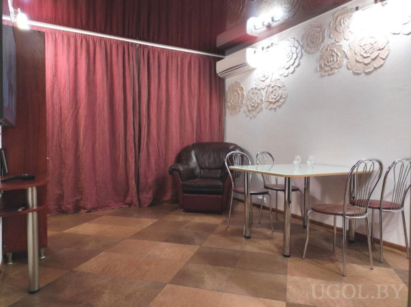 Кожаное кресло, стеклянный стол с четырьмя стульями, рельефная стена с подсветкой и красные шторы.