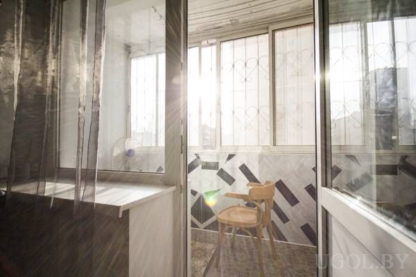 Закрытая лоджия с геометричной плиткой, деревянный стул, белый столик и решётки с узором в форме сердца.