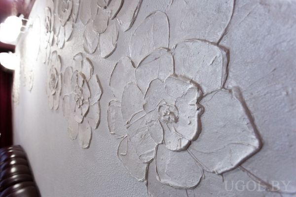 Объёмные цветы на светлой стене, акцентное освещение сбоку подчёркивает текстуру и глубину узора.
