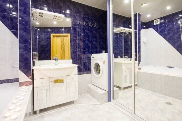 Стиральная машина на подиуме, белая тумба, ванна, синие и белые плитки, свечи и зеркальные двери.